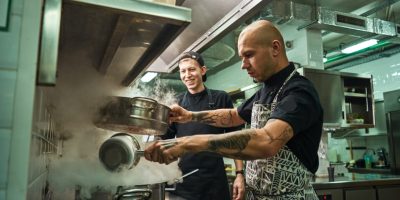 Culinary school. Handsome and confident chef teaching how to cook his two assistants in a restaurant kitchen. Cooking concept